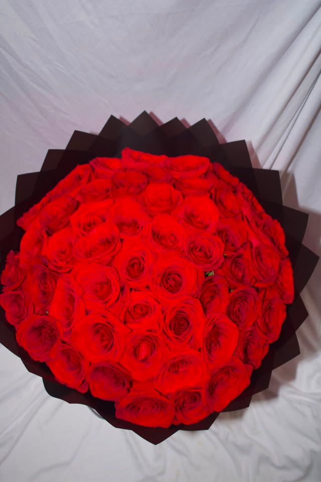 A large round bouquet of red roses wrapped in black paper