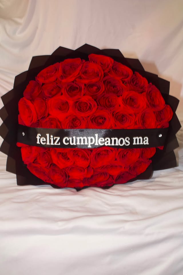 A red rose bouquet in black paper with a custom feliz cumpleanos ma ribbon