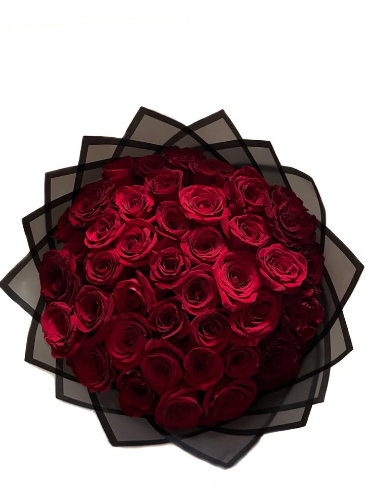 Deep red roses arranged in a full round bouquet wrapped in black mesh