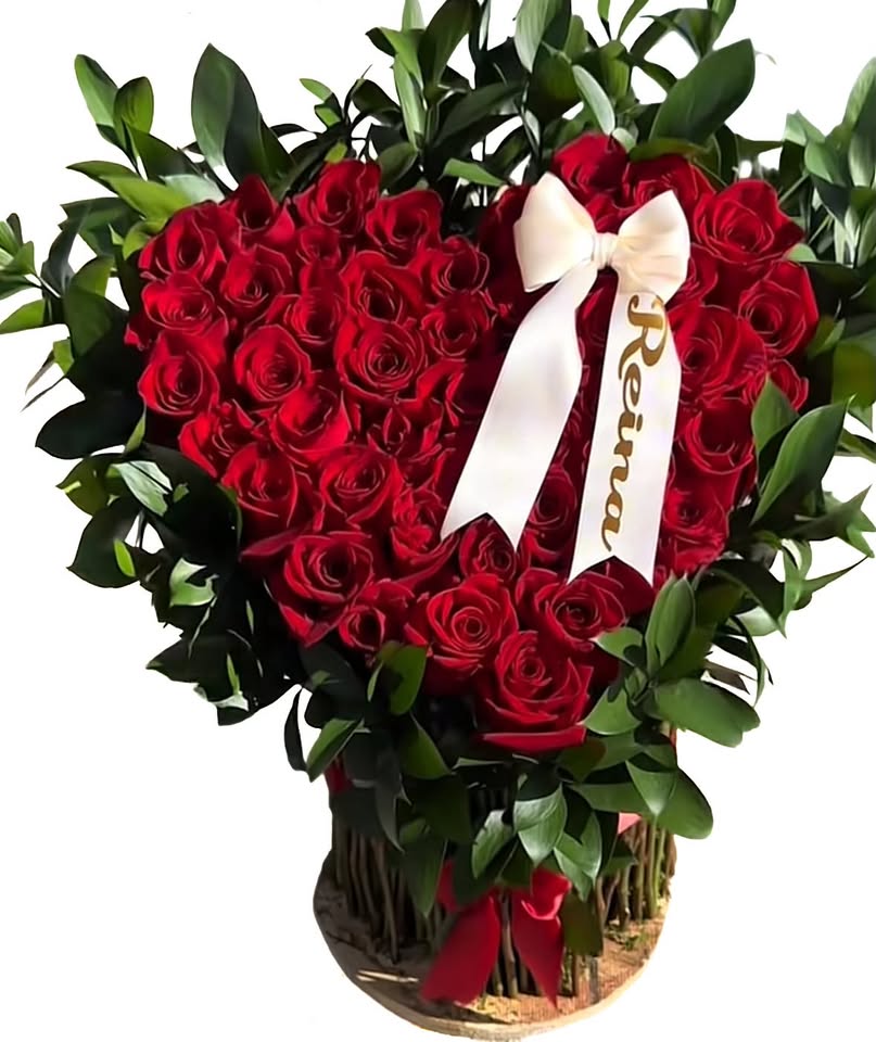 A heart-shaped arrangement of red roses with a white satin bow